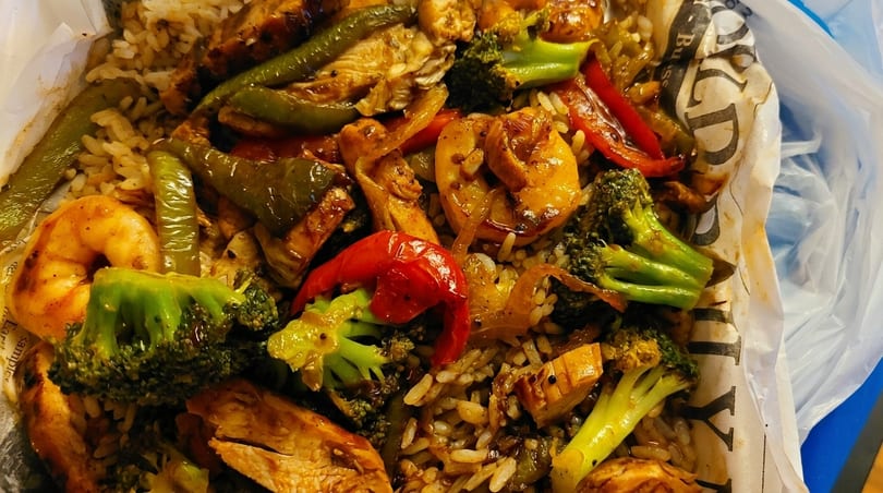Close-up of a stir-fry dish with rice, chicken, shrimp, broccoli, and bell peppers.