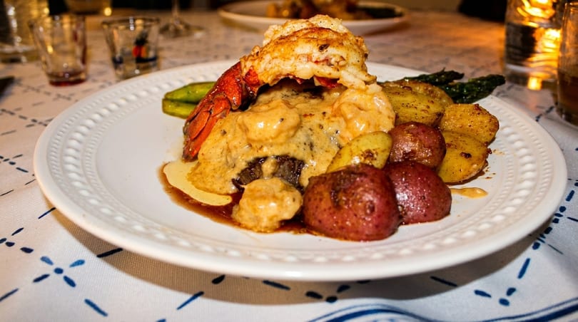 Lobster tail and steak with creamy sauce, roasted potatoes, and asparagus on a white plate.